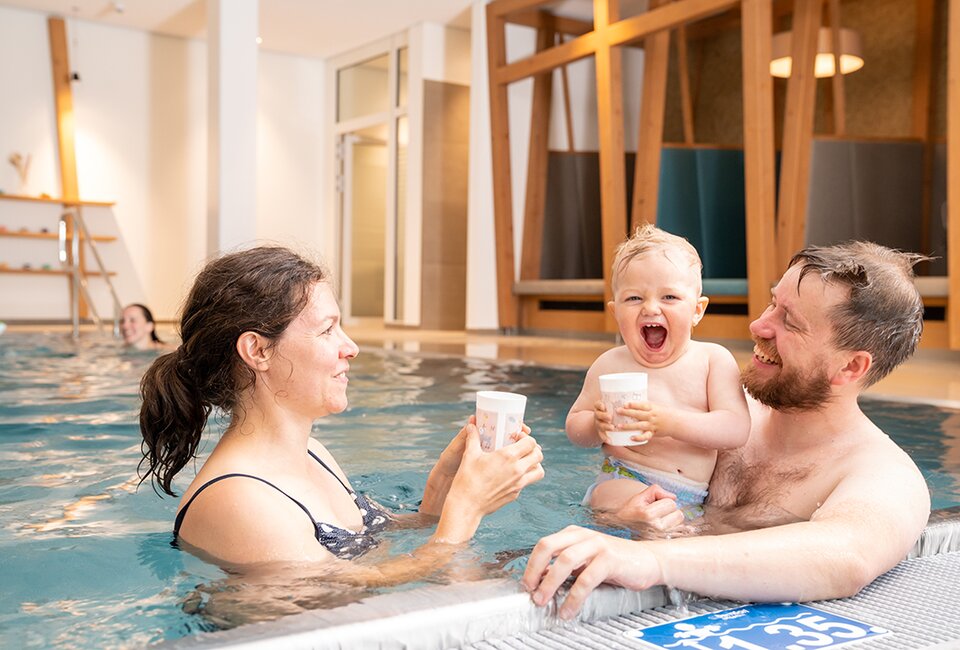 Familie mit Baby im Hallenbad, lachend mit den Schlüchtmühle-Bechern
